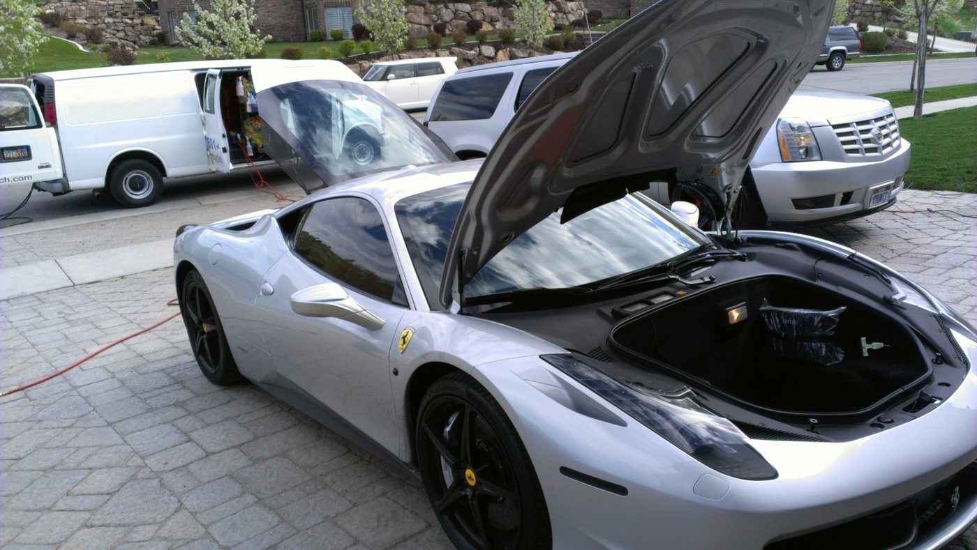 A detailer performing paint correction work on a red sports car in a professional workshop