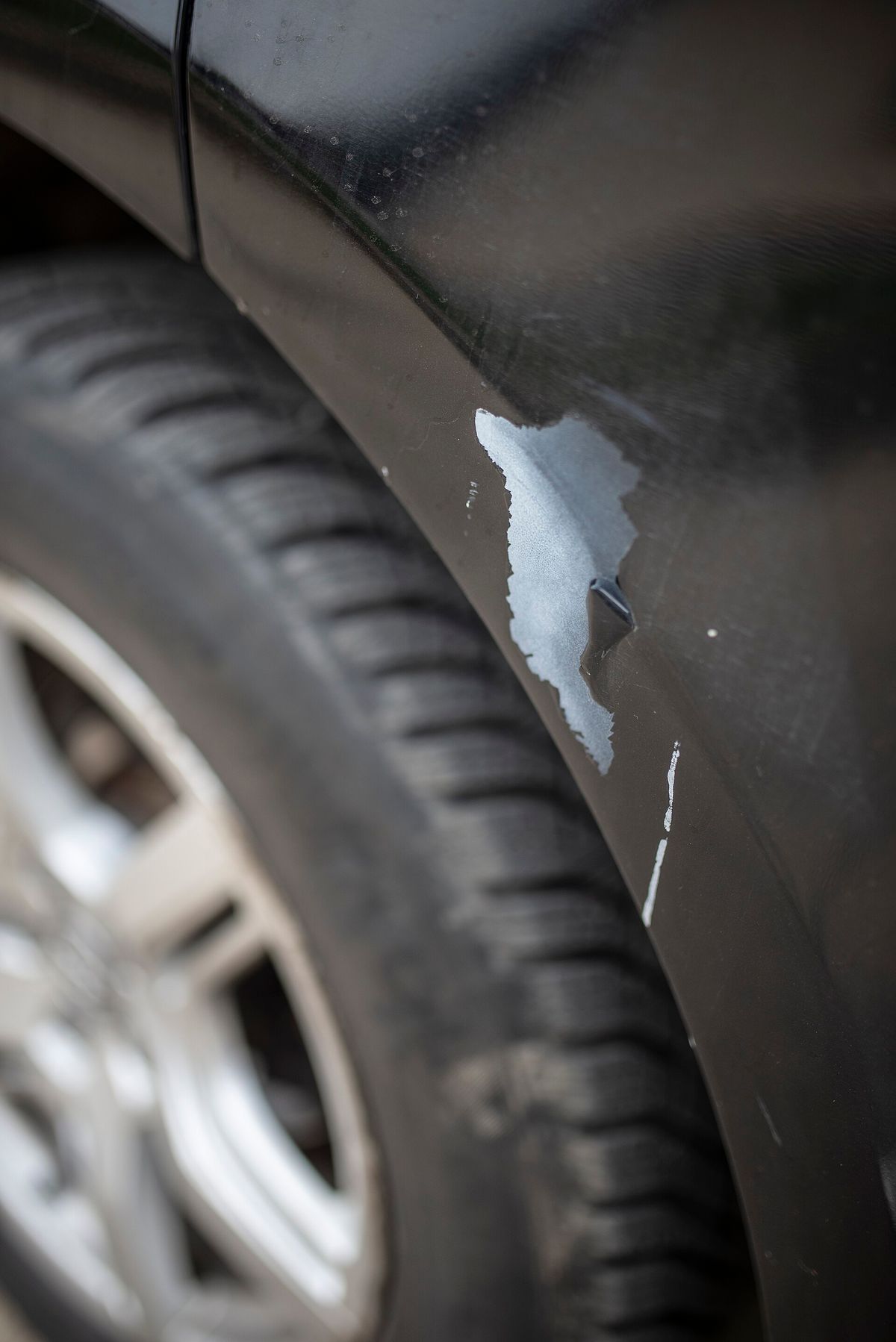 Close-up of scratches and missing paint on a car fender next to the tire