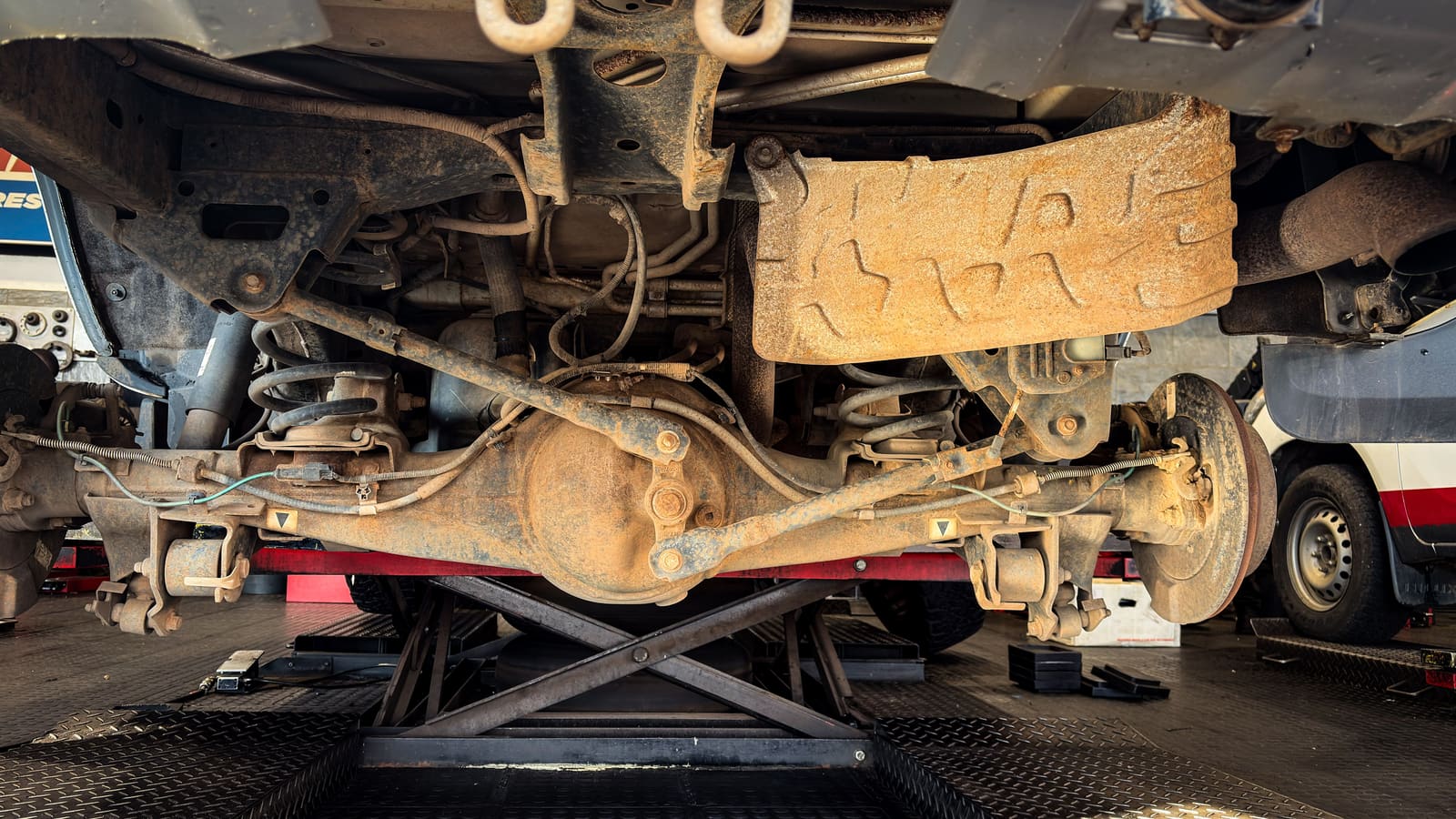 Rusted vehicle undercarriage and suspension being examined on a shop lift