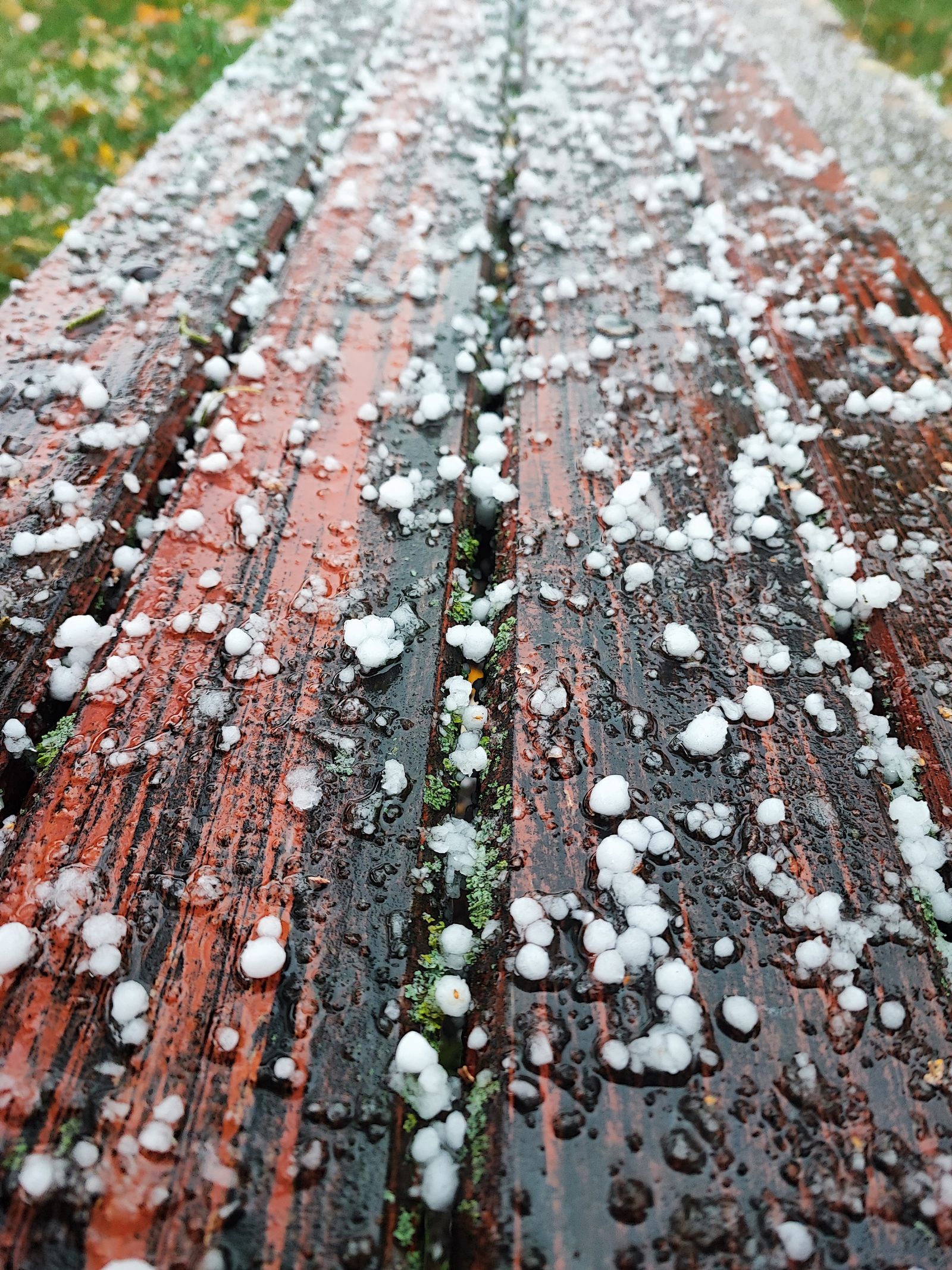 White hailstones scattered across a wet wooden deck after a storm