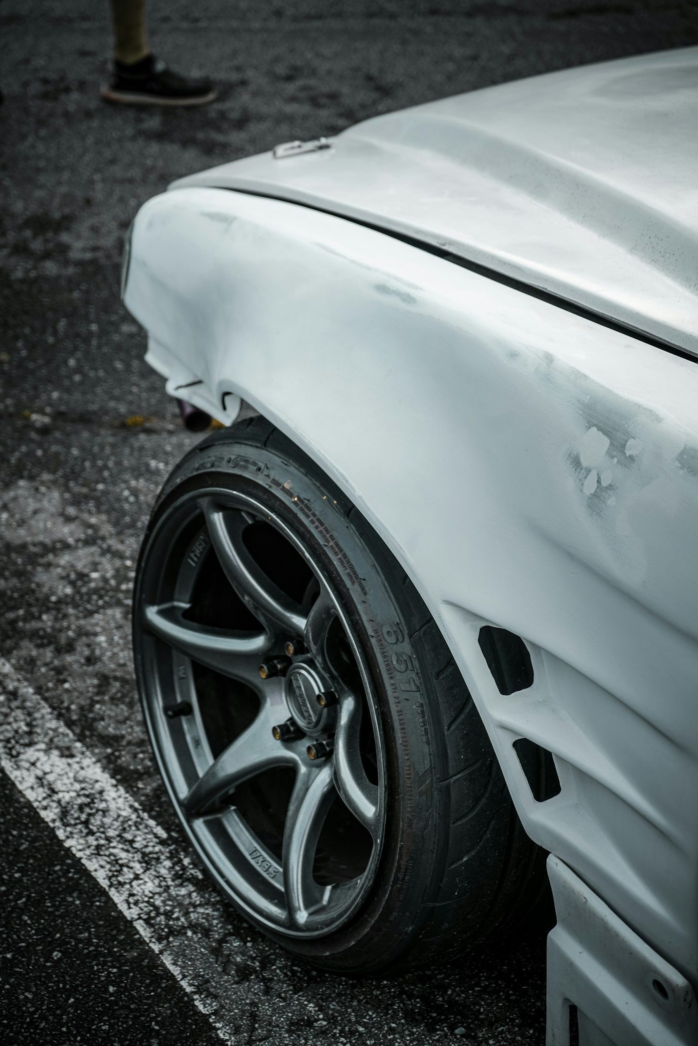 A white car with a visible dent in the hood parked in a parking lot