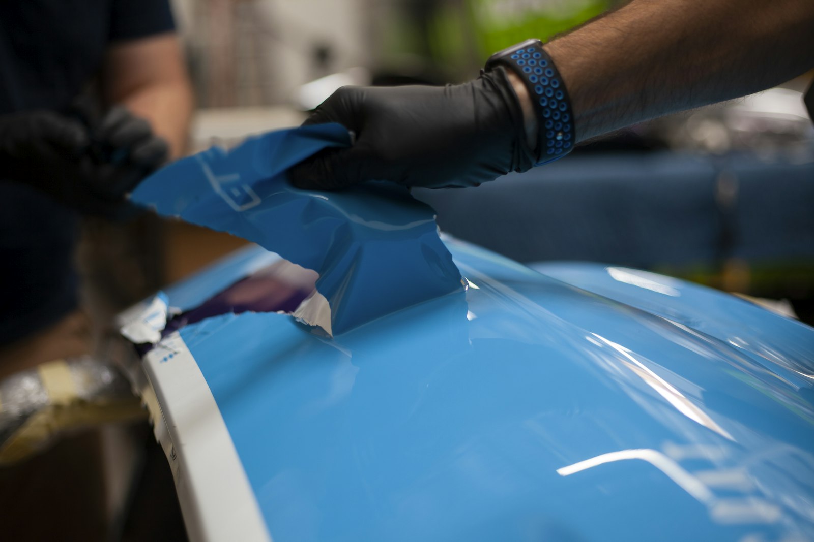 Technician wearing protective gloves applying a clear protective coating to a car body panel