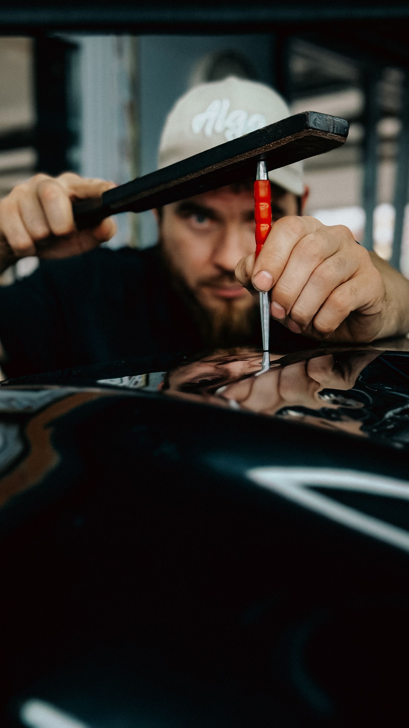 A technician using a tap-down paddle and a pick to work a dent out of a glossy black car panel