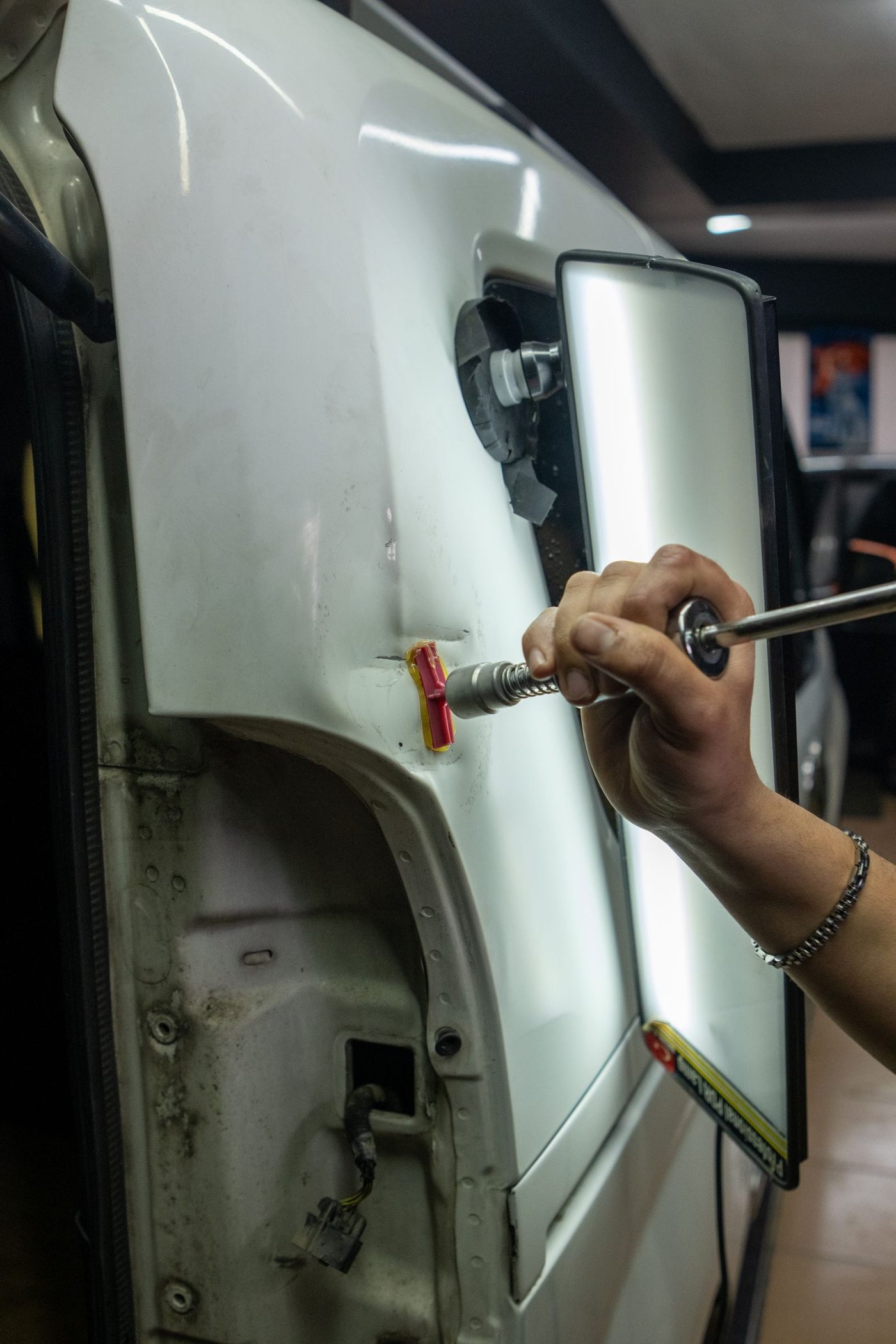 A technician's hand using a glue-pull tab and slide hammer tool on a fender panel in an auto body garage