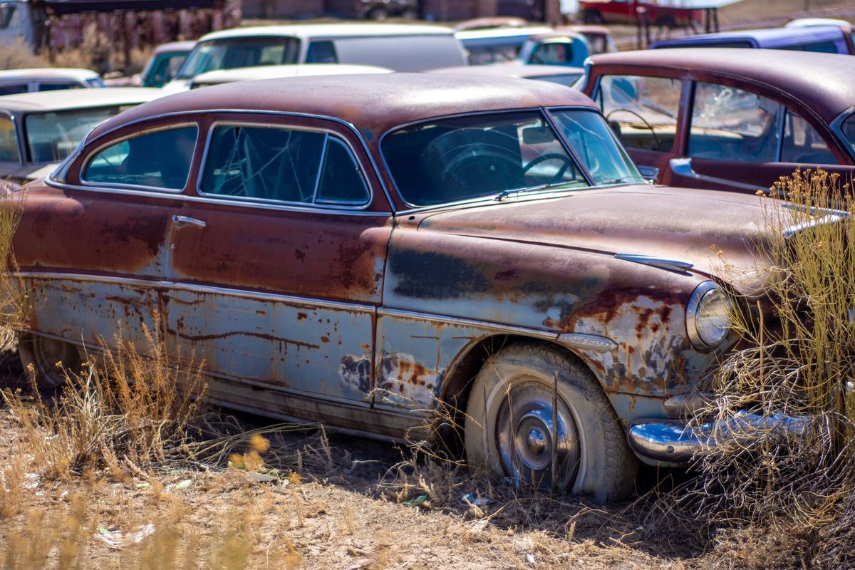 Close-up of a rusty, corroded classic car body in a junkyard