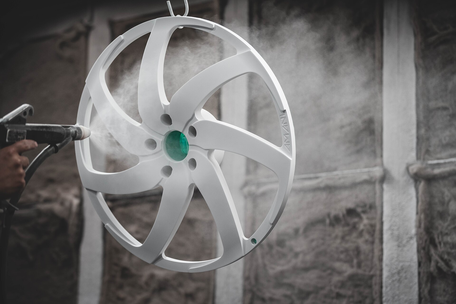 An alloy wheel face hanging on a hook being sprayed white inside a powder-coating booth