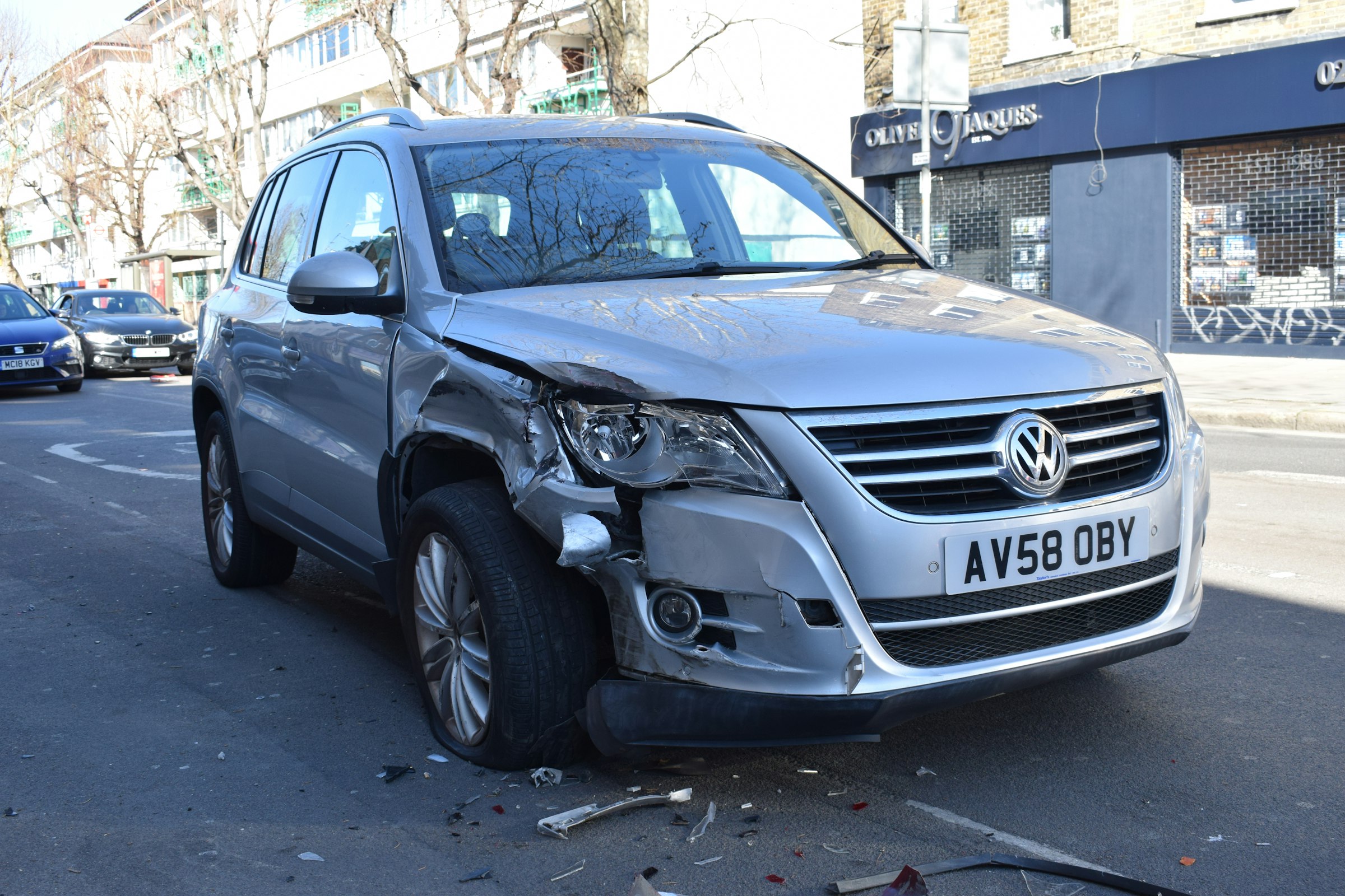 Close-up of a silver SUV with a crumpled front corner and torn bumper after a collision