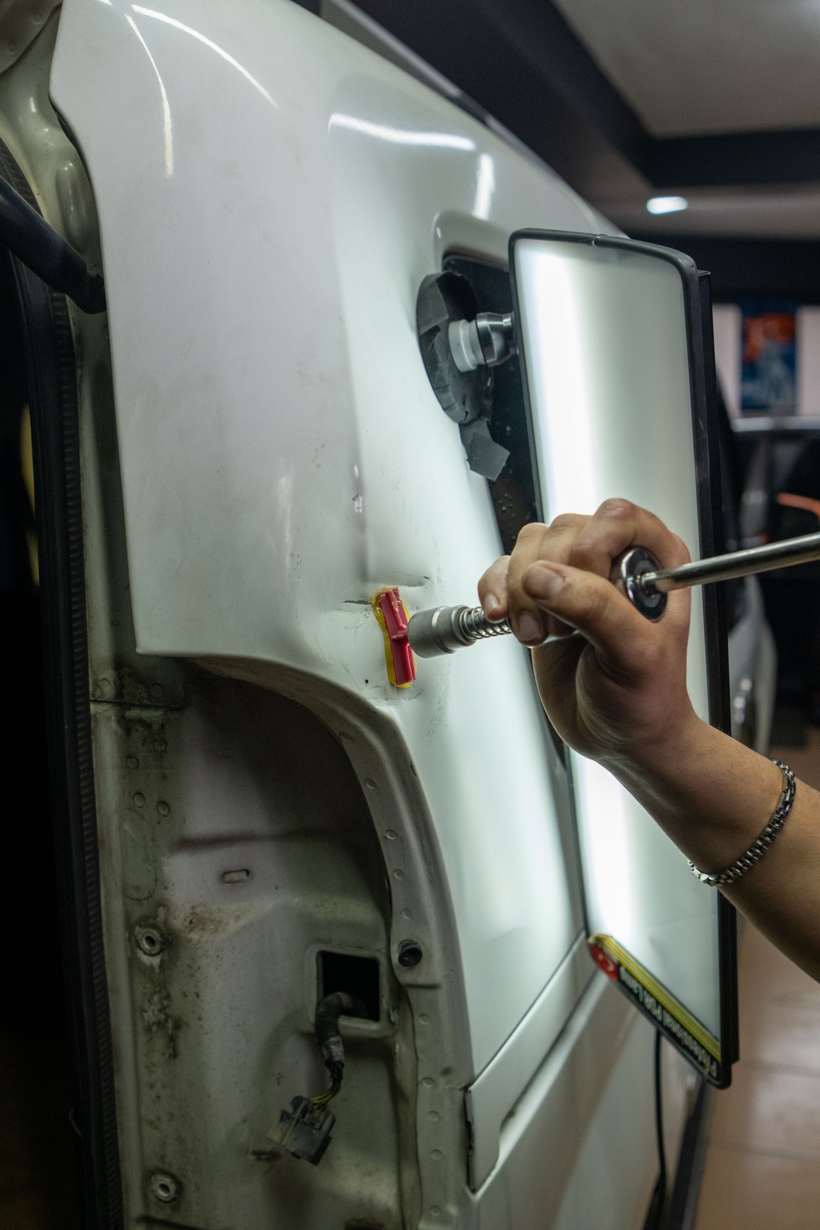 A technician using a glue-pull tab and slide hammer to work a dent on a vehicle's rear body panel above the wheel arch