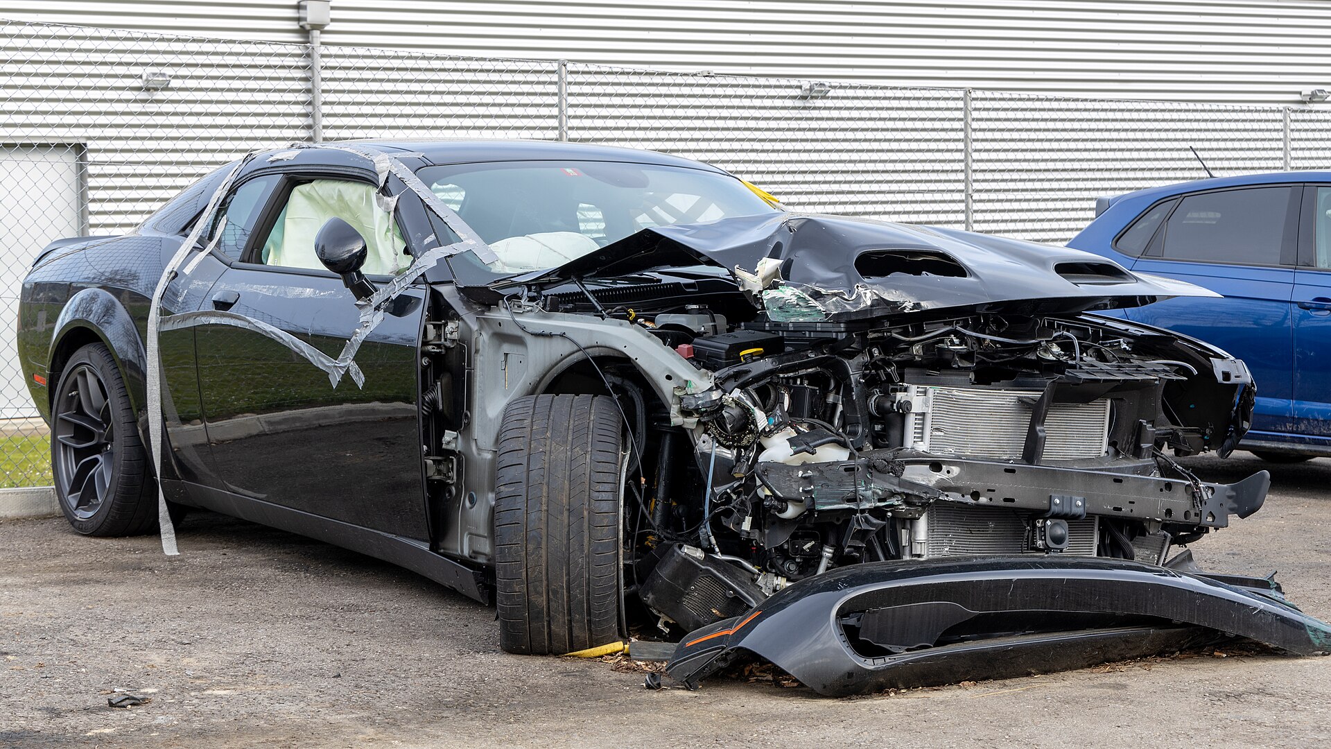 A black sports car with the entire front end torn open and the bumper detached after a severe collision