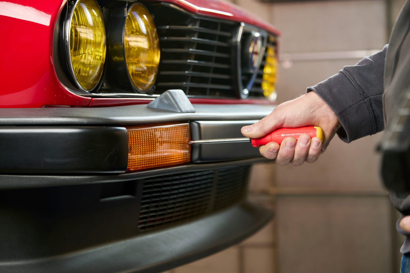 A mechanic using a screwdriver to work on a car's front bumper