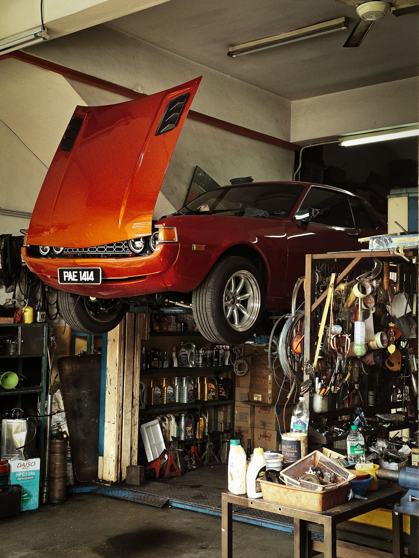 A classic coupe raised on a two-post lift in a cluttered independent repair shop