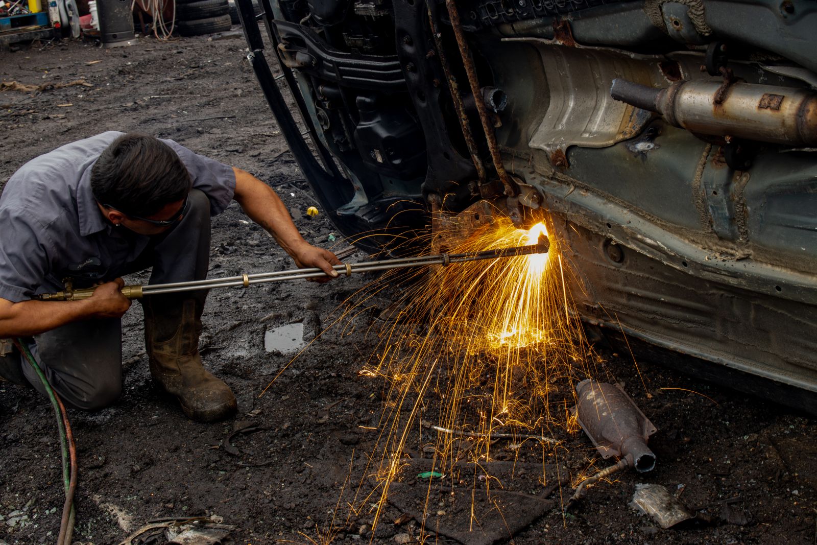 A worker using a cutting torch on the rusted underbody of a vehicle, sparks showering down
