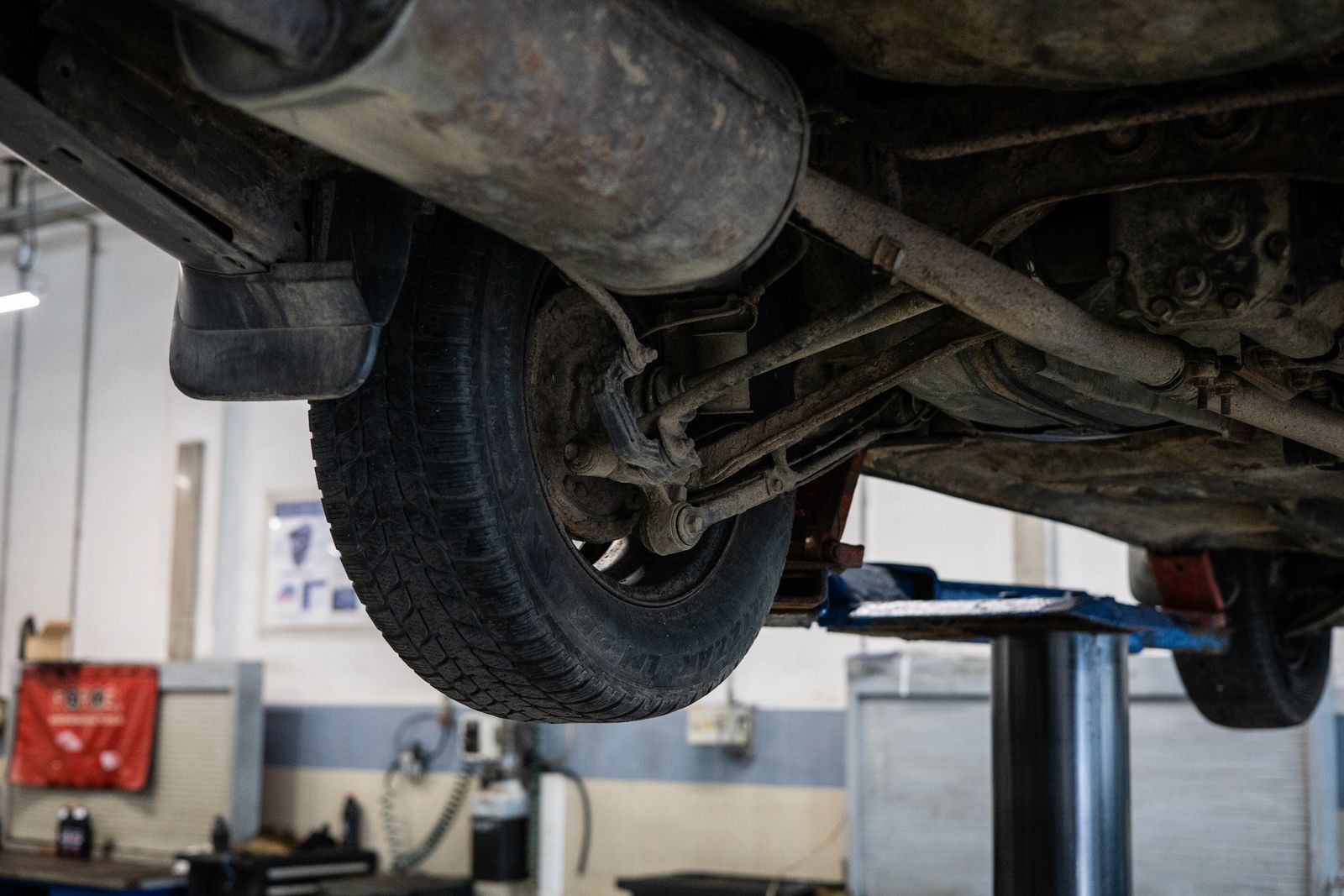 The underside of a vehicle raised on a two-post lift showing exhaust, suspension arms and surface rust