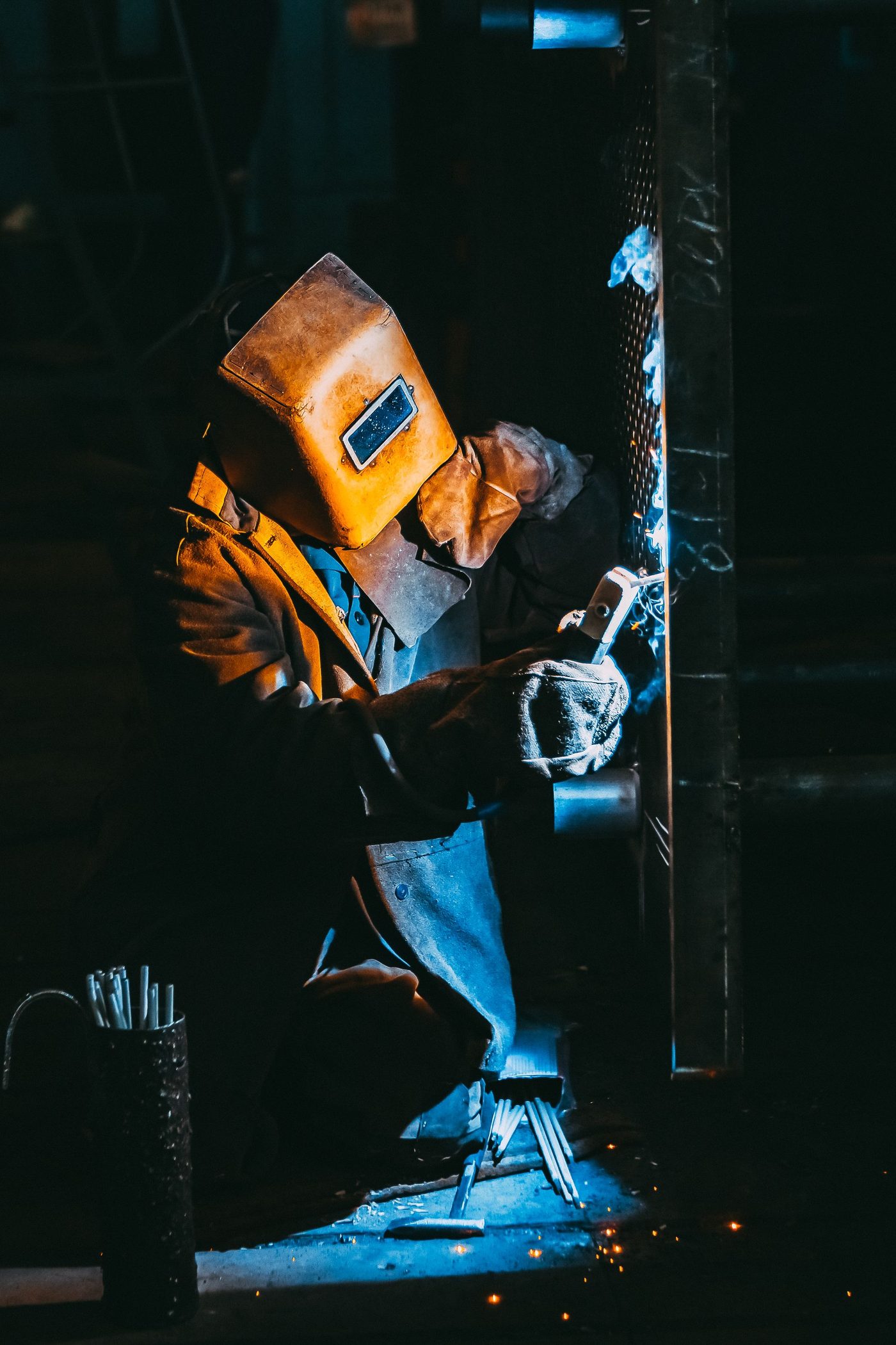 A welder in protective gear welding a piece of metal, sparks flying in a workshop