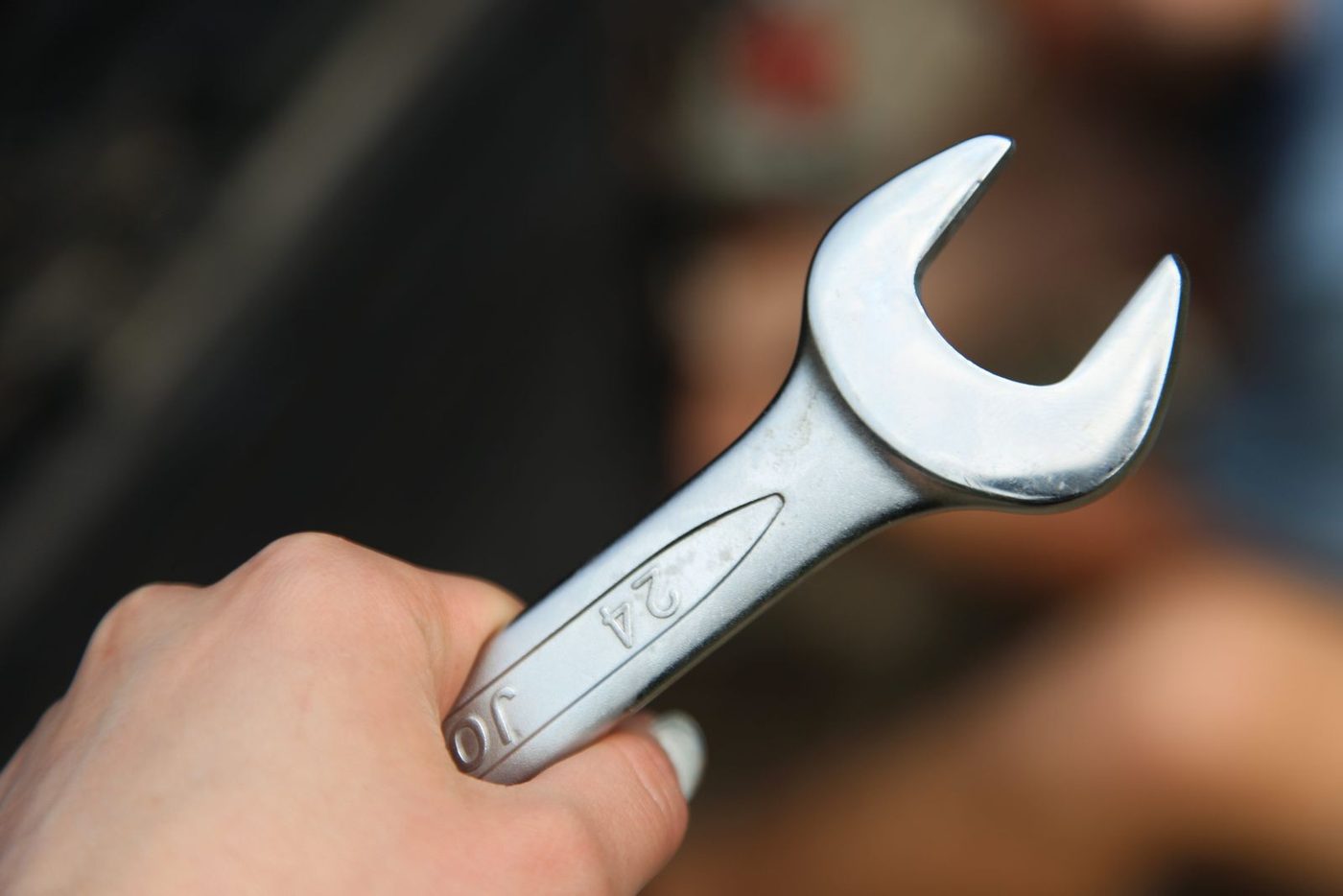 A close-up of a hand holding a metal wrench for automotive repair